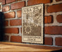 A wooden table with a brick wall in the background, and a metal sign with a floral design hanging on the wall.