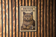 A British Shorthair cat is depicted on a British one-cent stamp, which is affixed to a wooden wall.