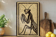 a framed illustration of a praying mantis, a type of insect, on a shelf next to a wooden cutting board and some lemons.