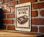 A sign with the text "DOUGH BOWL" is displayed on a brick wall, with a wooden table below it.