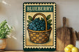 A vintage-style metal sign with a basket of blueberries, placed on a wooden shelf next to a wooden cutting board and a potted plant.
