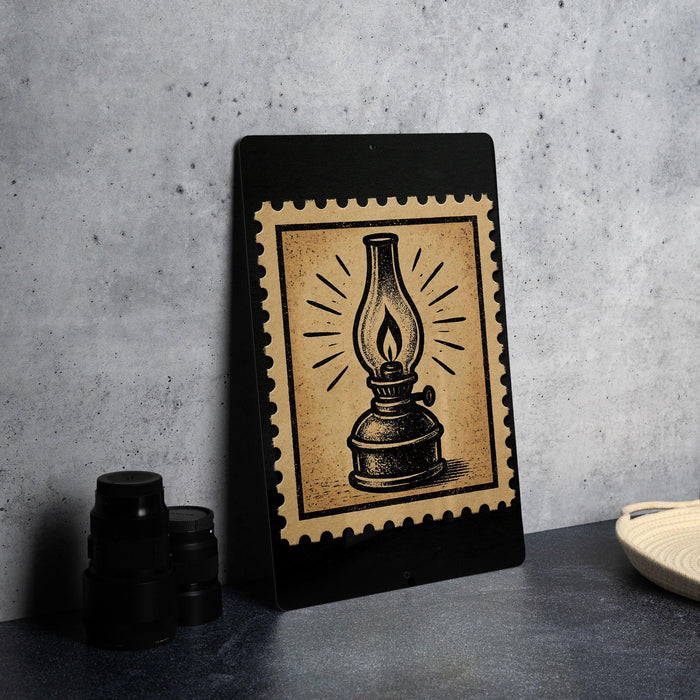 a black frame with a vintage-style illustration of a lantern on it, placed on a dark surface next to some black camera lenses.