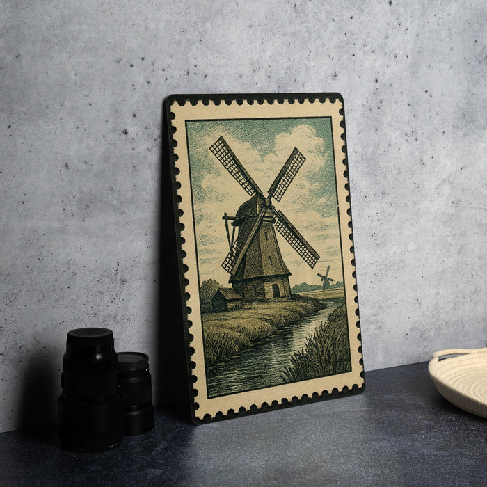 A framed illustration of a windmill is displayed on a table, accompanied by a stack of black camera lenses and a white dish.