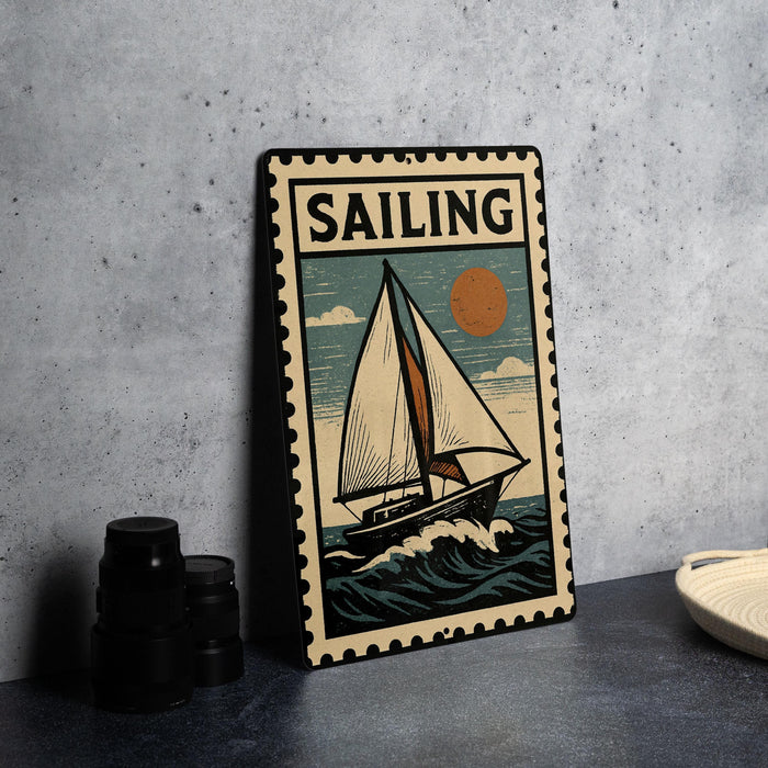A vintage-style metal sign with a sailboat illustration and the word "SAILING" prominently displayed, placed on a dark surface against a concrete wall.