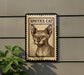 a postage stamp-like sign with a portrait of a Sphynx cat, mounted on a wall next to a plant.