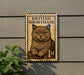 A British Shorthair cat is depicted on a postage stamp-like sign, mounted on a wall.