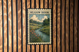 A framed illustration of a river with flowers and trees, mounted on a wooden wall.