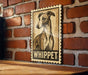 A wooden table with a framed illustration of a dog, specifically a whippet, on a brick wall.