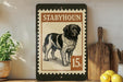 A framed illustration of a dog, likely a Stabhoun, is displayed on a shelf next to a wooden cutting board and some kitchen utensils.