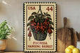 A framed stamp depicting a hanging basket of fuchsia flowers, with the text "USA 44 FUCHSIA HANGING BASKET" printed on it. The stamp is placed on a shelf next to a wooden cutting board and a potted plant.