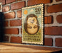 A vintage-style postage stamp featuring a smiling hedgehog, mounted on a brick wall.