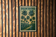 A framed image of palm trees is displayed on a wooden wall.