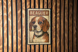 A metal stamp-like sign with a picture of a beagle dog and the word "BEAGLER" printed on it, mounted on a wooden wall.