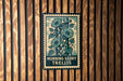 A wooden wall with a framed poster featuring a plant with large green leaves and a flower.