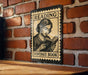 A vintage-style metal sign with a woman reading a book, mounted on a brick wall.