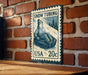 A vintage-style postage stamp depicting a person riding a snow tube, mounted on a brick wall.