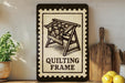 a framed illustration of a quilting frame, with a potted plant to the left and a wooden cutting board to the right.