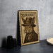 A wooden postcard with a rabbit wearing a hat and coat, sitting on a table next to some black camera lenses.