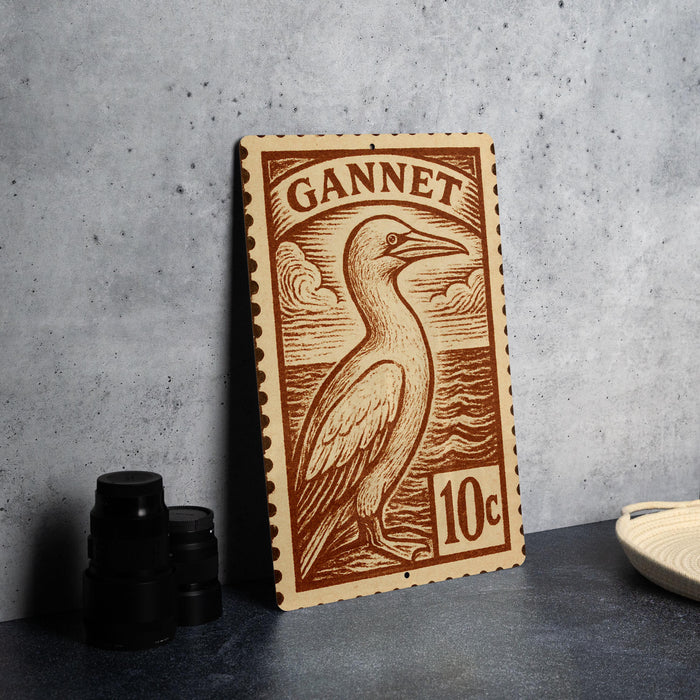 a wooden postcard or stamp with a bird illustration, placed on a table next to some black camera lenses.