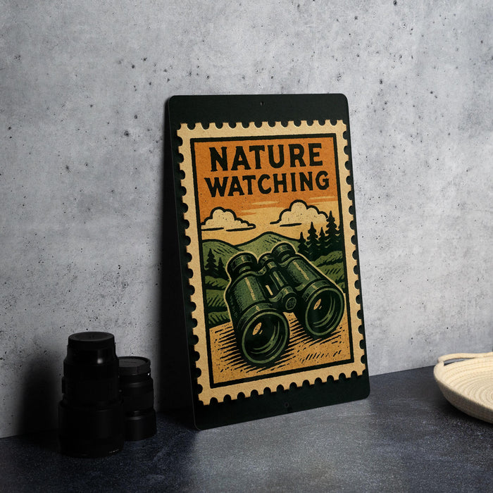 A metal sign with a vintage-style illustration of binoculars and the text "NATURE WATCHING" is displayed on a table.