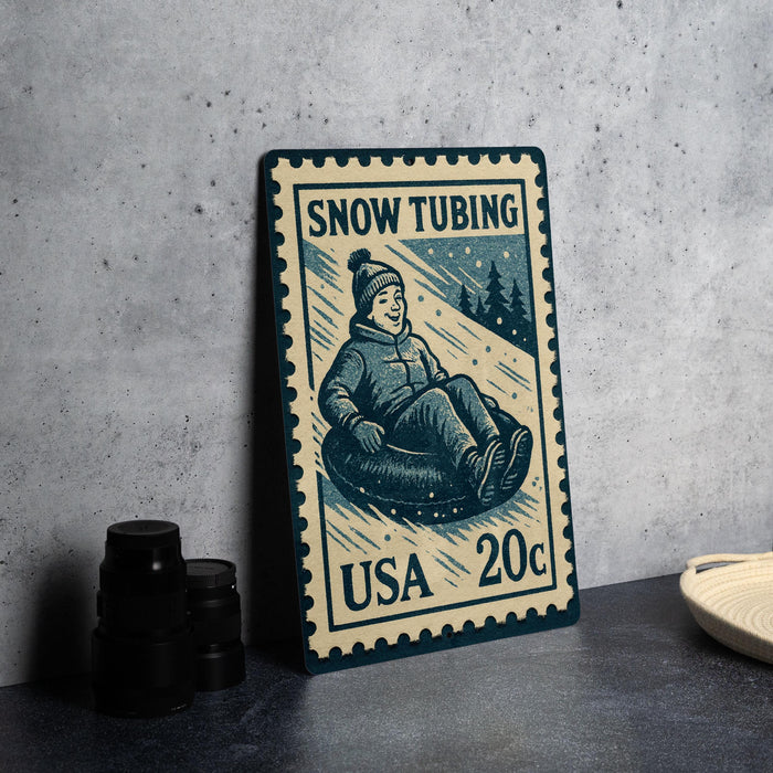 A vintage-style postage stamp depicting a person riding a sled or toboggan, with the text "SNOW TUBING USA 20c" printed on it.