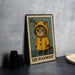 A metal stamp depicting a cat wearing a yellow raincoat, standing in the rain.