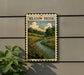 a framed illustration of a scenic landscape with a river, flowers, and trees, mounted on a wall.