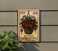 A postage stamp featuring a hanging basket of fuchsia flowers, mounted on a wall next to a plant.