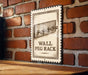 A metal sign with a drawing of a peg rack mounted on a brick wall.