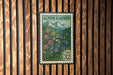 A postage stamp from the United States, featuring a mountain landscape with flowers, is displayed on a wooden wall.
