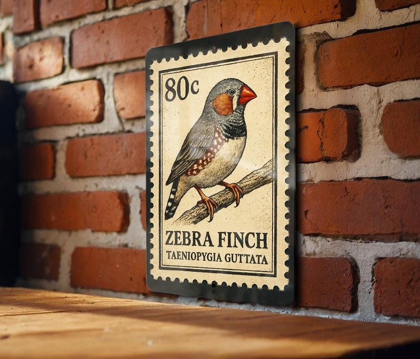 A metal postage stamp featuring a detailed illustration of a zebra finch perched on a branch, with the text "Zebra Finch" and "Tæeniopygia gutta" printed on it.
