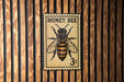 A metal stamp with a bee illustration on it, mounted on a wooden wall.