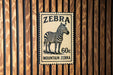 A vintage-style stamp featuring a zebra, with the text "Zebra" and "60c" printed on it, mounted on a wooden wall.