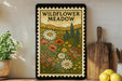 a framed illustration of a wildflower meadow, with various flowers and plants depicted in a decorative and artistic style.