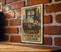 A vintage-style metal sign with a floral illustration is mounted on a brick wall, displaying the text "WINDOW BOX GARDEN".