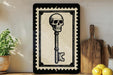 a framed illustration of a skull with a key, placed on a shelf next to a wooden cutting board and some lemons.