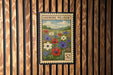 A postage stamp featuring a field of colorful flowers, including red, white, and purple flowers, against a wooden background.