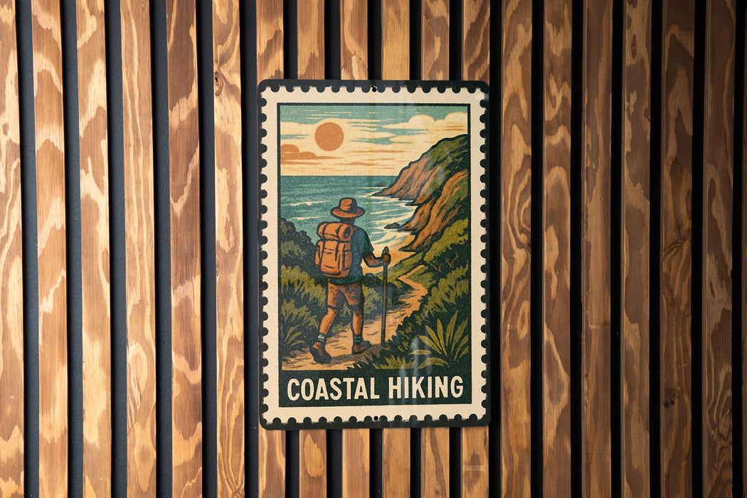 A coastal hiking sign is displayed on a wooden wall, featuring a hiker walking along a trail with a scenic backdrop of the ocean and mountains.
