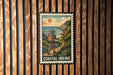 A coastal hiking sign is displayed on a wooden wall, featuring a hiker walking along a trail with a scenic backdrop of the ocean and mountains.