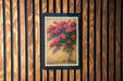A framed painting of a vibrant floral arrangement is displayed on a wooden wall.