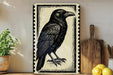 a black and white illustration of a crow, which is displayed on a wall next to a wooden cutting board and some potted plants.
