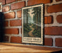 A metal sign with a forest trail illustration is mounted on a brick wall.