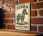 A vintage-style stamp featuring a zebra illustration, mounted on a brick wall.