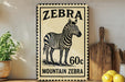 A vintage-style metal sign featuring a zebra illustration and the text "Zebra Mountain Zebra 60c" is displayed on a wooden shelf.
