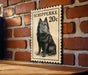 A black and white illustration of a dog, likely a Schipperke breed, is mounted on a brick wall.