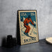 A vintage-style postage stamp featuring a skier in an orange suit, with the word "Skiing" written on it. The stamp is placed on a gray surface next to some black camera lenses.