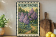 A framed postage stamp depicting a lush garden scene with purple flowers, placed on a shelf next to a wooden cutting board and some potted plants.