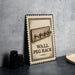 A wall peg rack sign is displayed on a table, with a stack of black camera lenses and a woven basket nearby.