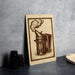 a wooden sign with an illustration of a metal container, possibly a teapot or a smoking device, on a gray wall.