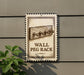 a wall-mounted sign with a wooden peg rack depicted on it, mounted on a gray wall.